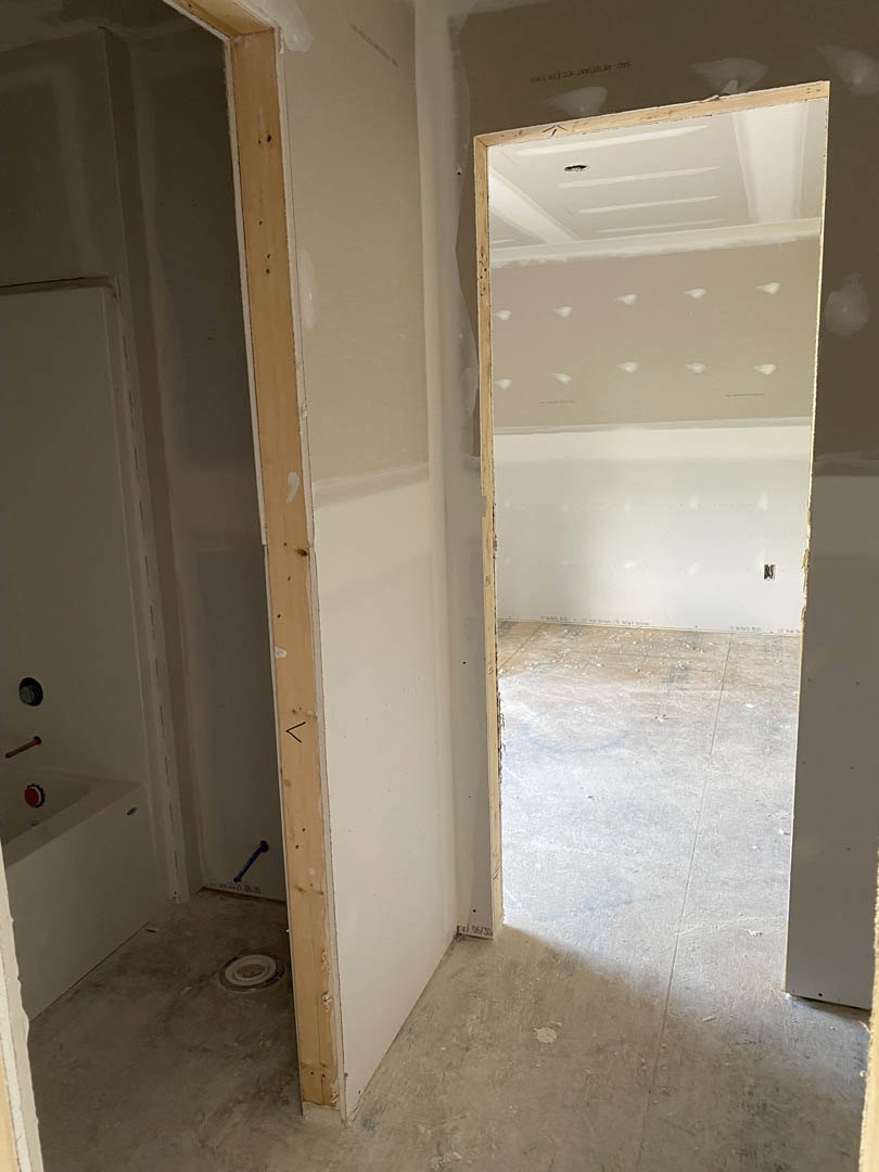 Bathroom with white tile flooring, open door, freestanding bathtub, white plaster walls, red door handle, recessed ceiling lights