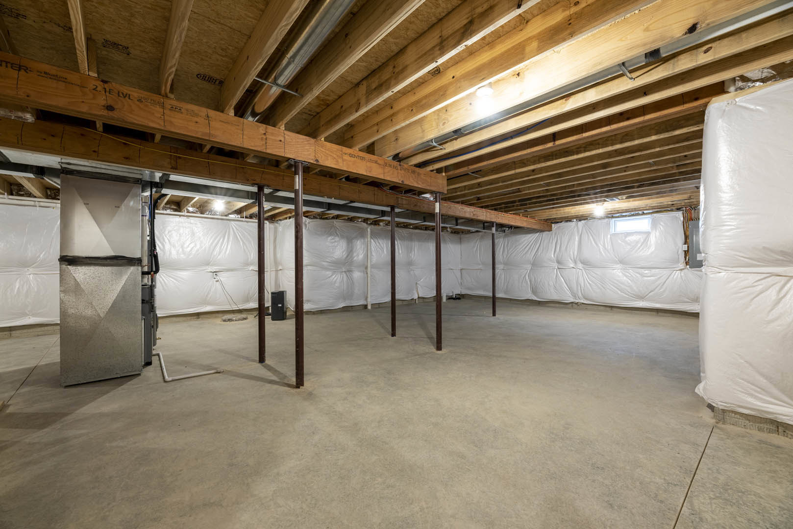 Exposed wood ceiling beams, white drywall, unfinished concrete floor, visible pipes and building insulation in a basement room