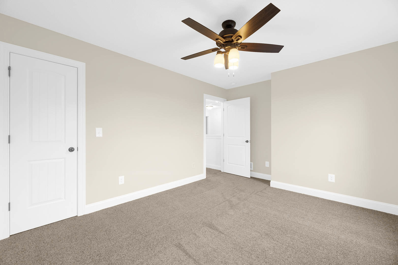 Ceiling fan with integrated lights above carpeted floor, white doors with silver knobs, plaster walls, and neutral interior finishes