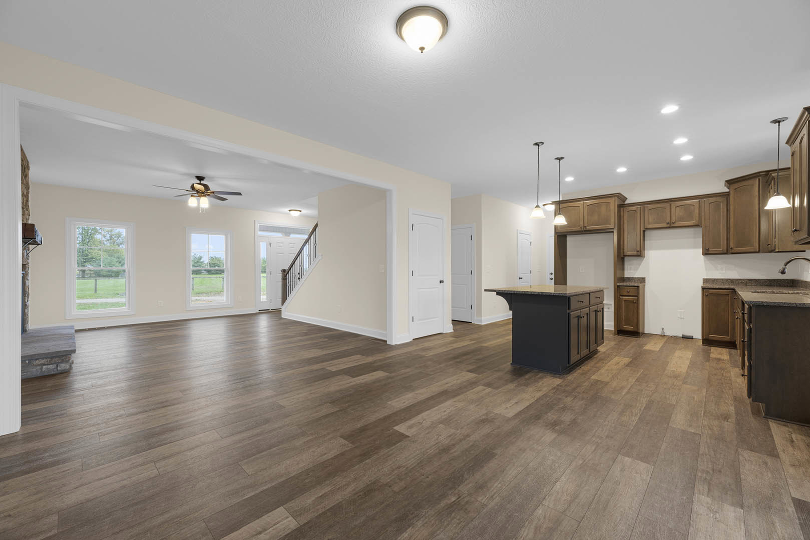 Spacious open floor plan featuring a kitchen island with granite countertops, hardwood floors, white walls, ceiling fan with lights, window overlooking a green lawn, and a white