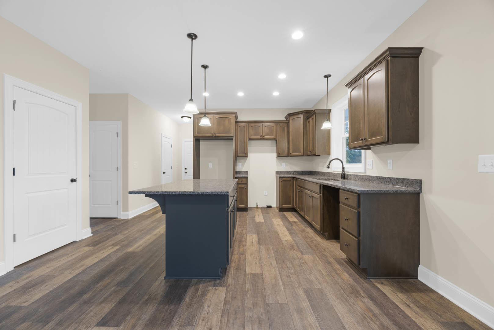 Kitchen with wood flooring, white cabinetry, black countertop island, stainless steel sink, and white doors featuring black and silver hardware