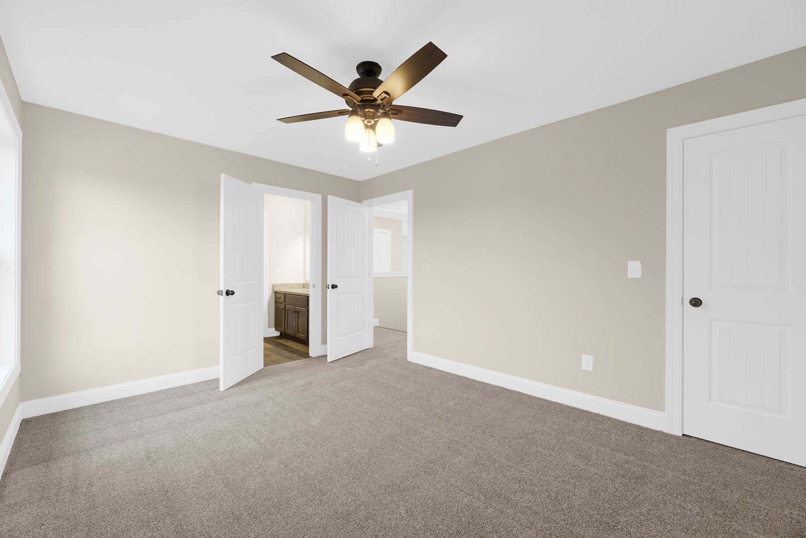 Carpeted room with white paneled doors featuring black knobs, ceiling fan with light fixture, neutral walls, and white crown molding