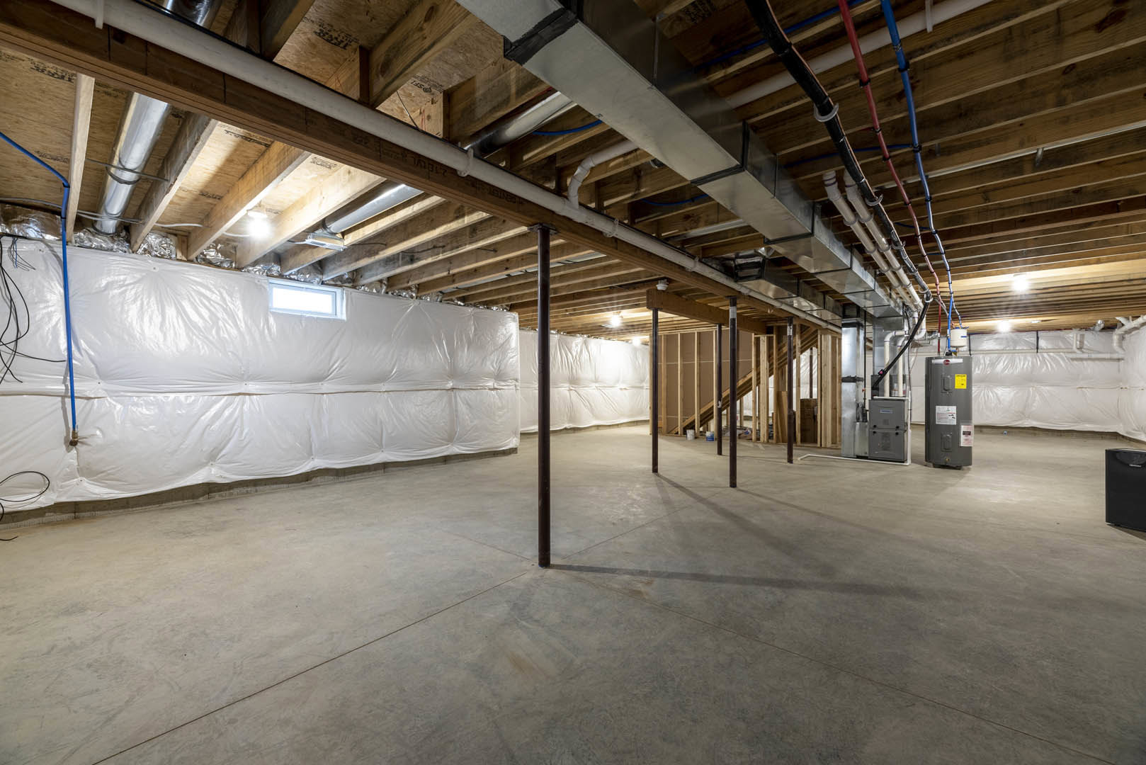 Basement with exposed steel pipes and beams, concrete floor, white walls, metal utility box, black wire, and ceiling light fixture