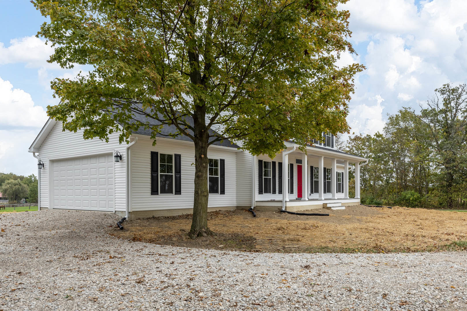 White house exterior with black shuttered windows, white frames, gravel landscaping, and a leafy green tree in front