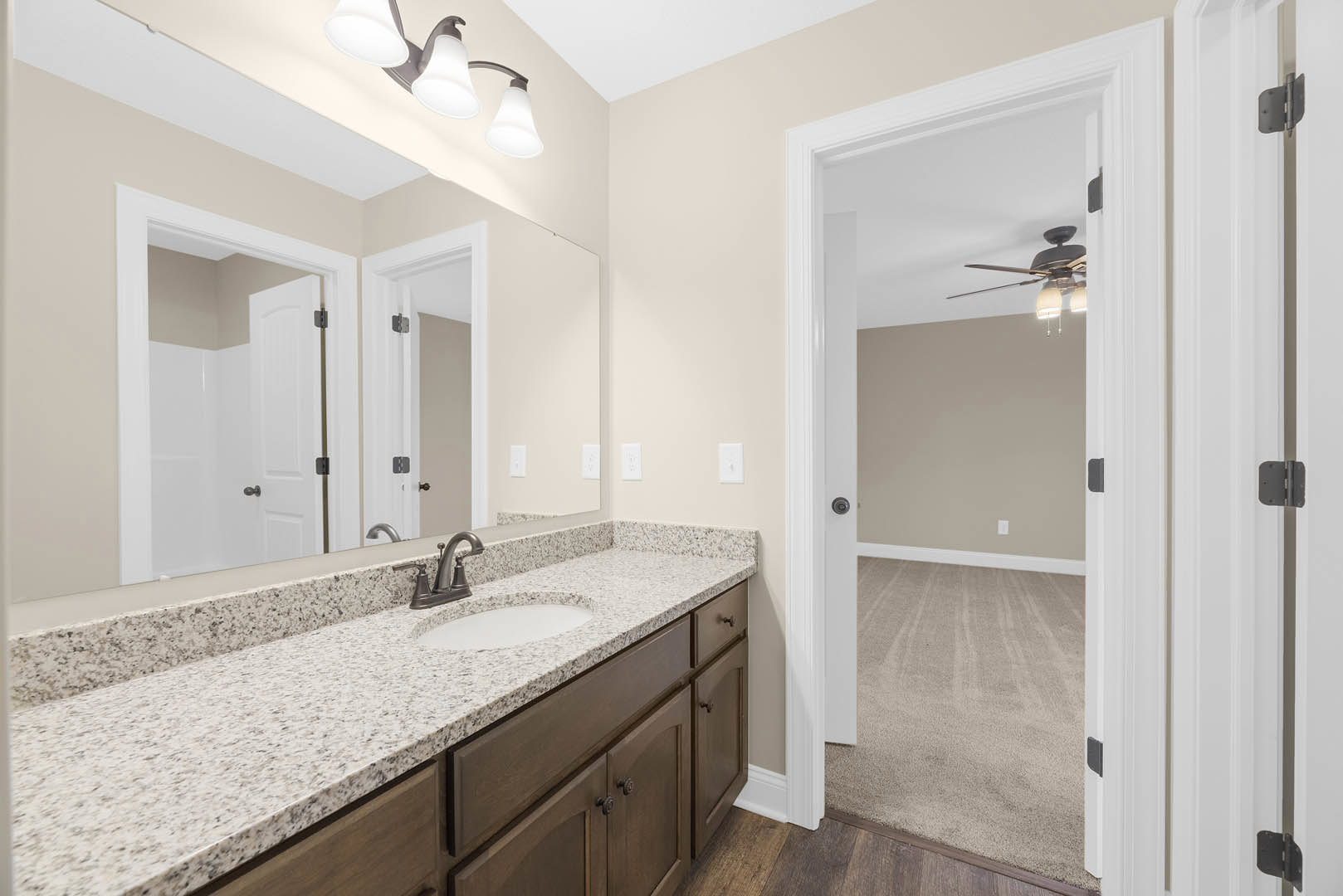Bathroom with marble countertop, undermount sink, chrome faucet, large mirror, ceiling fan, white door with silver handle, and tile flooring