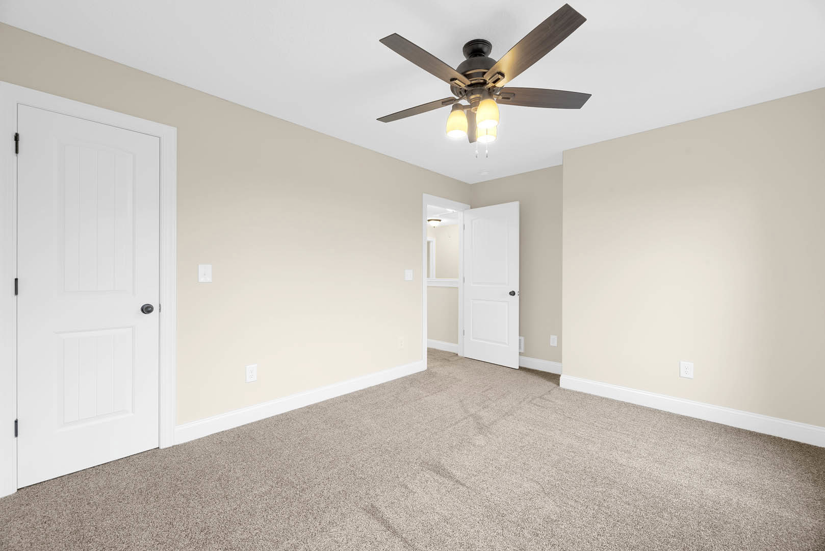 Ceiling fan with lights mounted above carpeted room, white walls and trim, white door with black handles and white frame