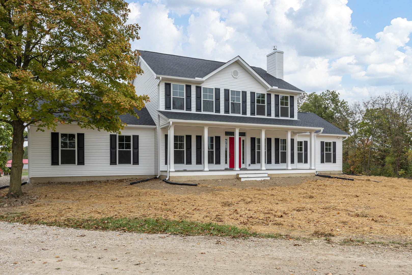 Large white house with black trim, red front door, black shuttered windows, dirt path leading to porch, mature tree beside exterior