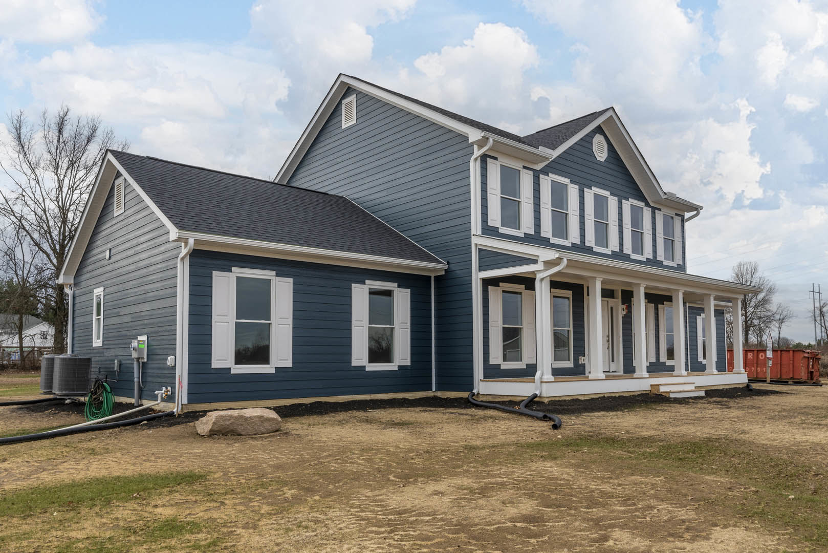 Blue siding house with white-framed windows, spacious grassy front yard, large decorative rock, and white shutters on windows