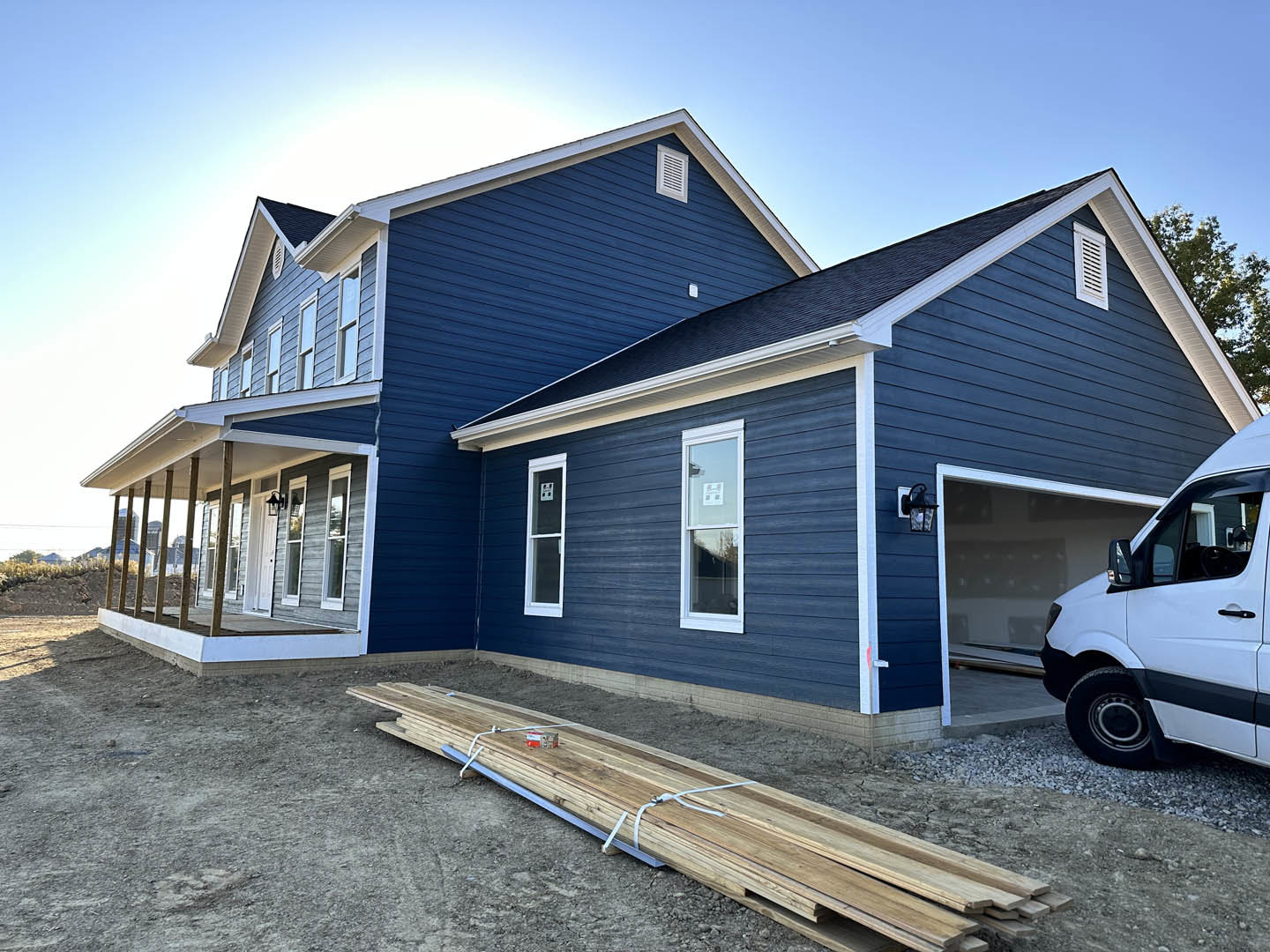 Blue house with white trim, attached garage, white truck parked in driveway, stack of wood pallets near entrance, windows with white frames, clear sky overhead