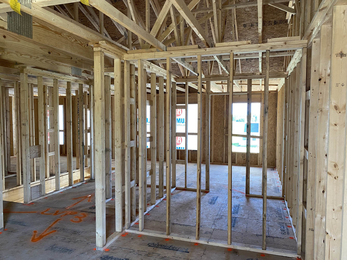 Exposed wood ceiling beams, large windows, and unfinished walls in a custom home interior under construction