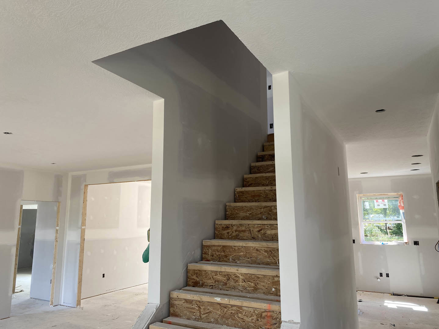 Open staircase with wooden treads and white risers, adjacent to a plaster wall and wood beam, large window with signage, doorway featuring a wall-mounted mirror, and wood panel
