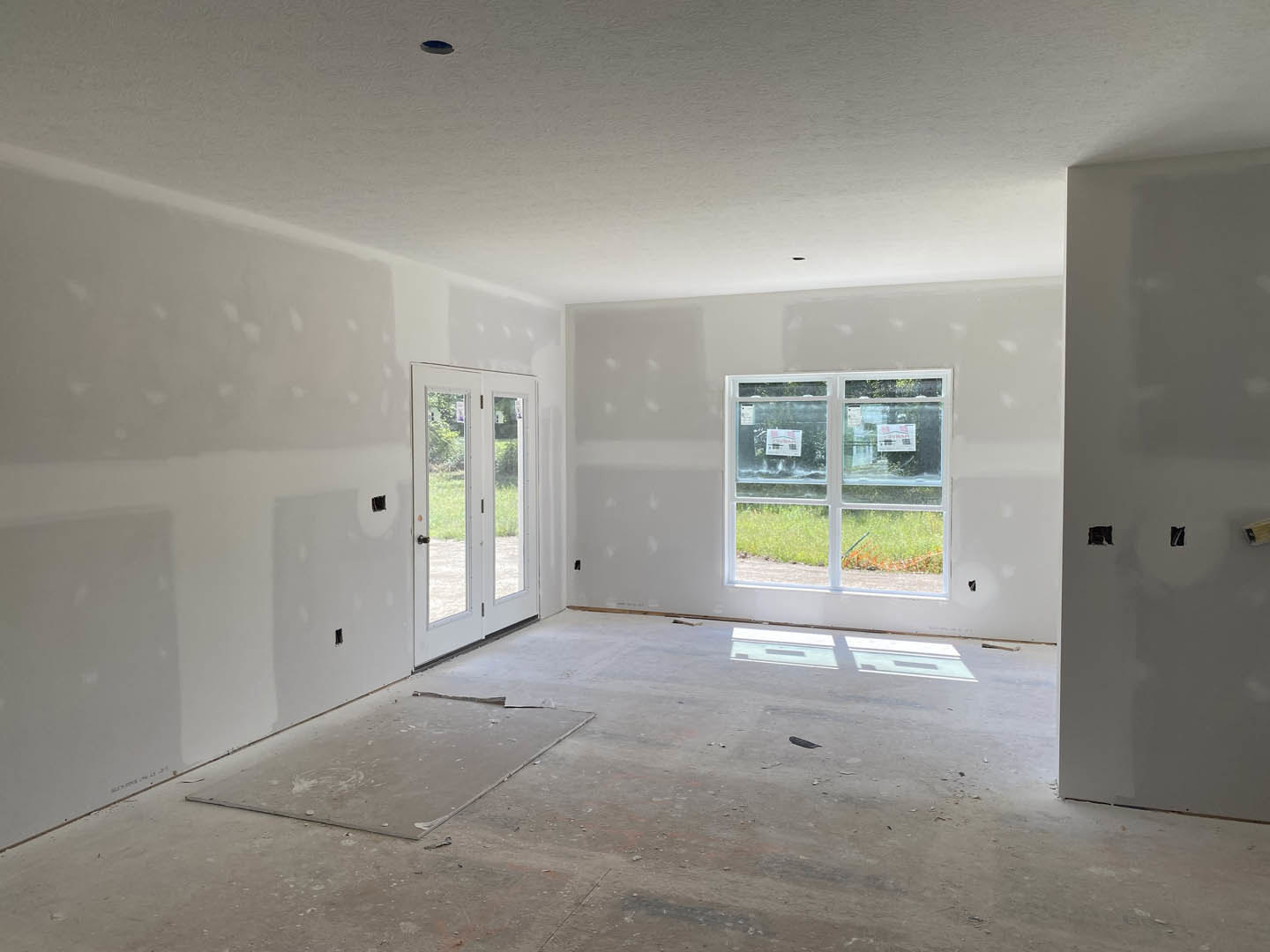 White-walled room featuring a glass-paneled white door, window with signage and shadow, light-colored flooring, and a single chair placed centrally.