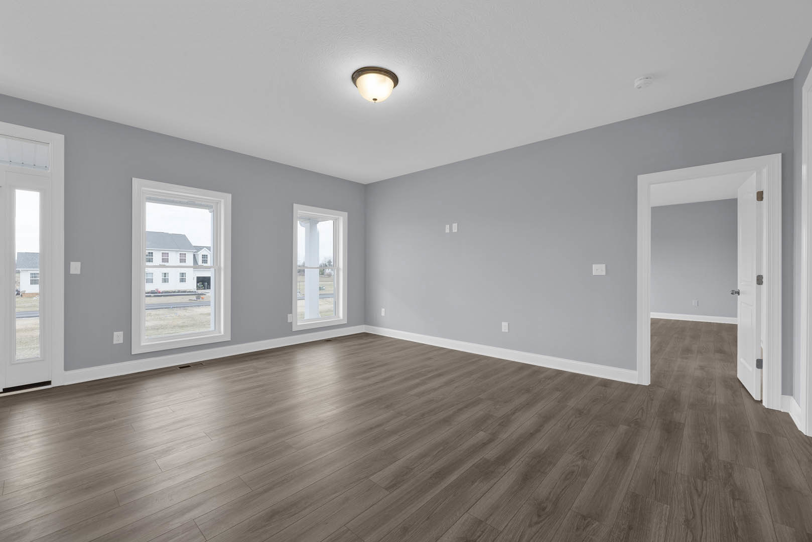 Hardwood floor in a bright room with white-framed windows, white door with glass panel, plaster walls, and ceiling light fixture