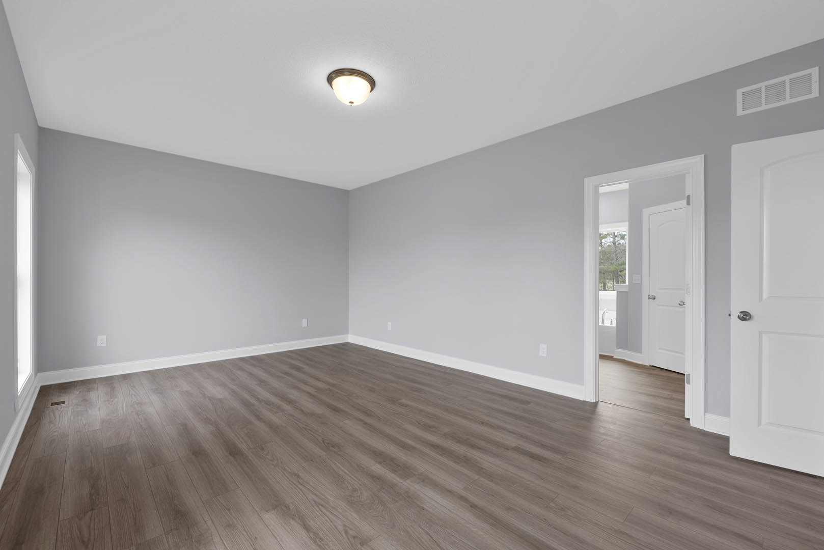 Wood flooring with white baseboard trim, white door featuring silver knobs, ceiling vent, and modern light fixture.