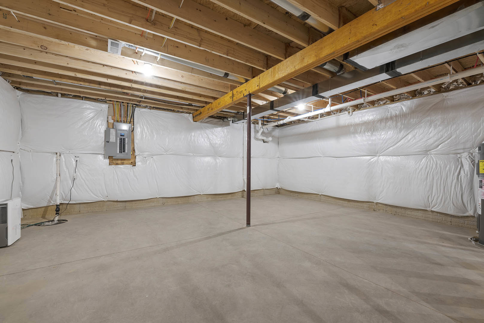 Basement room with exposed wooden ceiling beams, white plaster walls, concrete floor, visible metal pole, white vent, and building insulation.