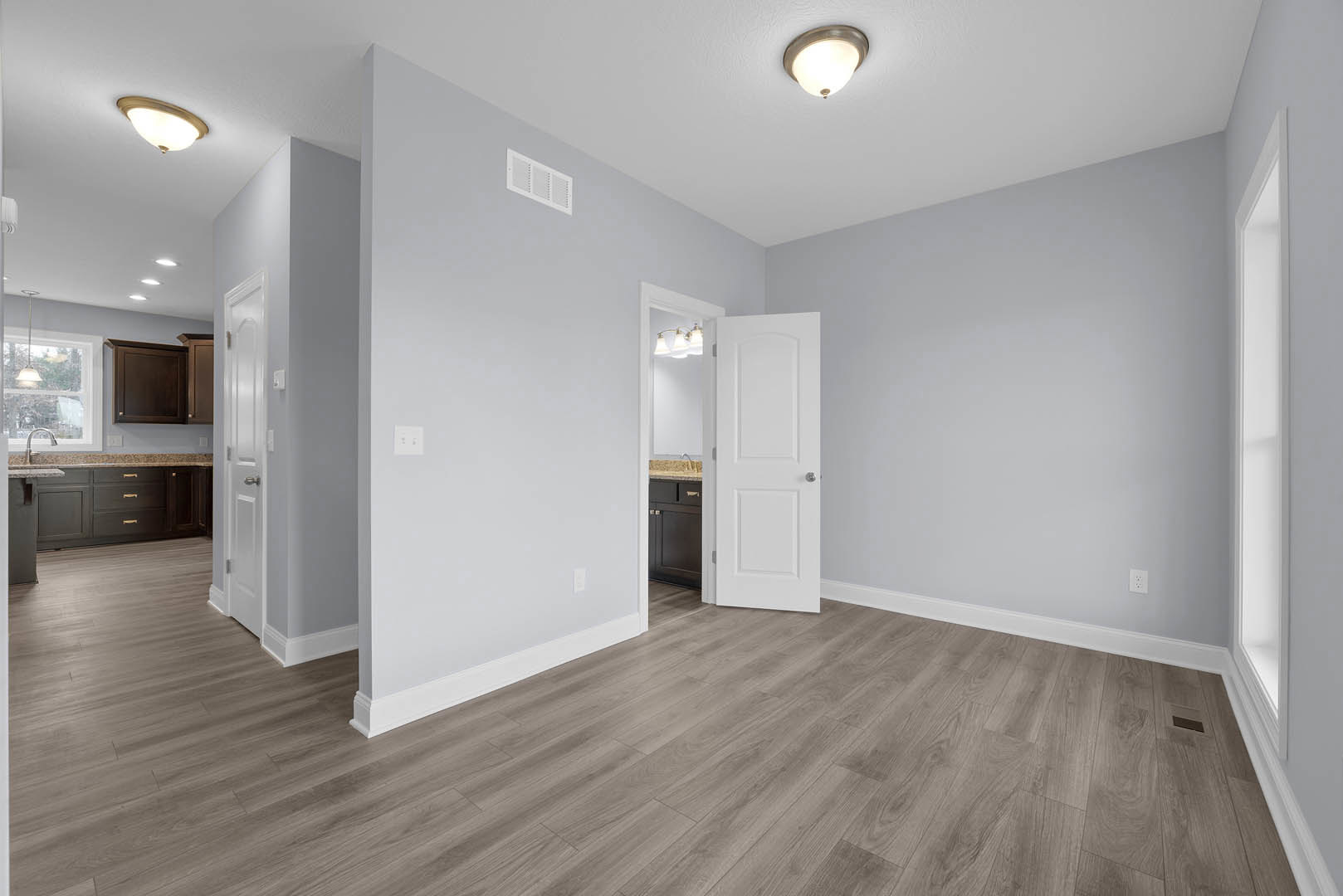 White paneled door with silver knob opens into a room featuring light wood laminate flooring, white baseboard trim, plaster walls, ceiling-mounted light fixture, and a white wall