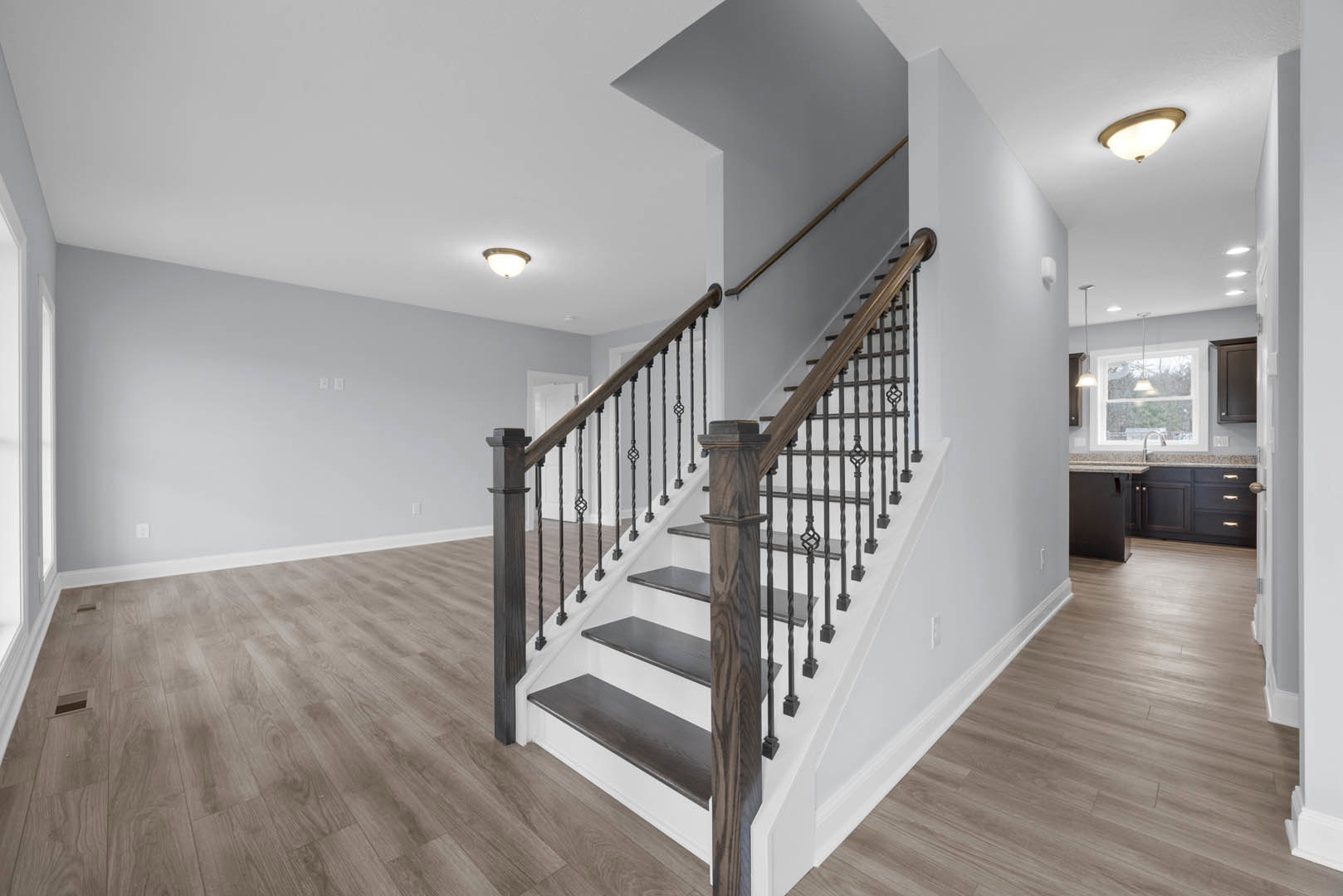 Wood staircase with matching railings, laminate flooring, plaster walls, ceiling light fixture, door partially visible, window overlooking leafy trees