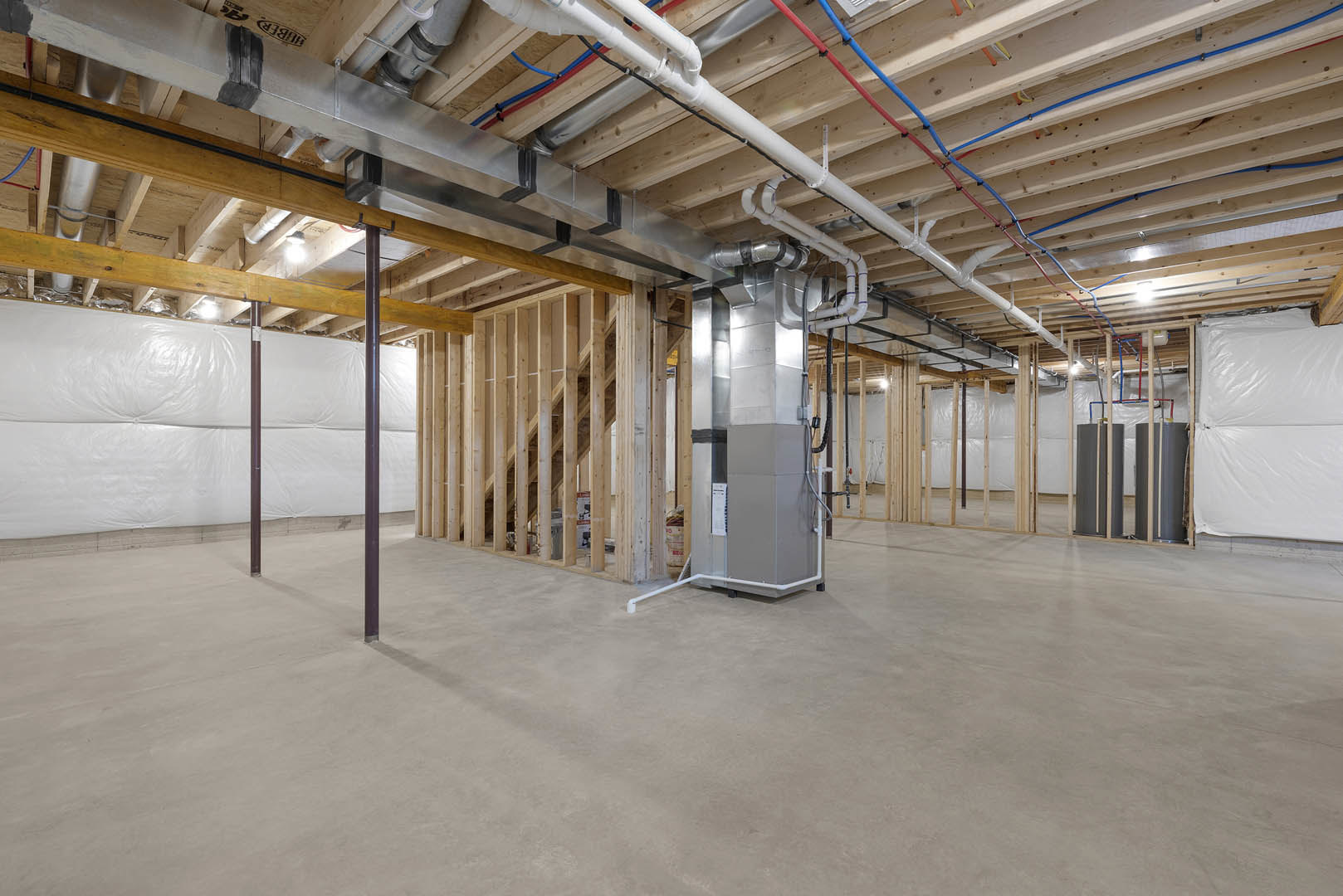 Exposed steel beams, pipes, and wires run along the unfinished basement ceiling and walls, with white plastic sheeting covering sections and a grey refrigerator positioned against