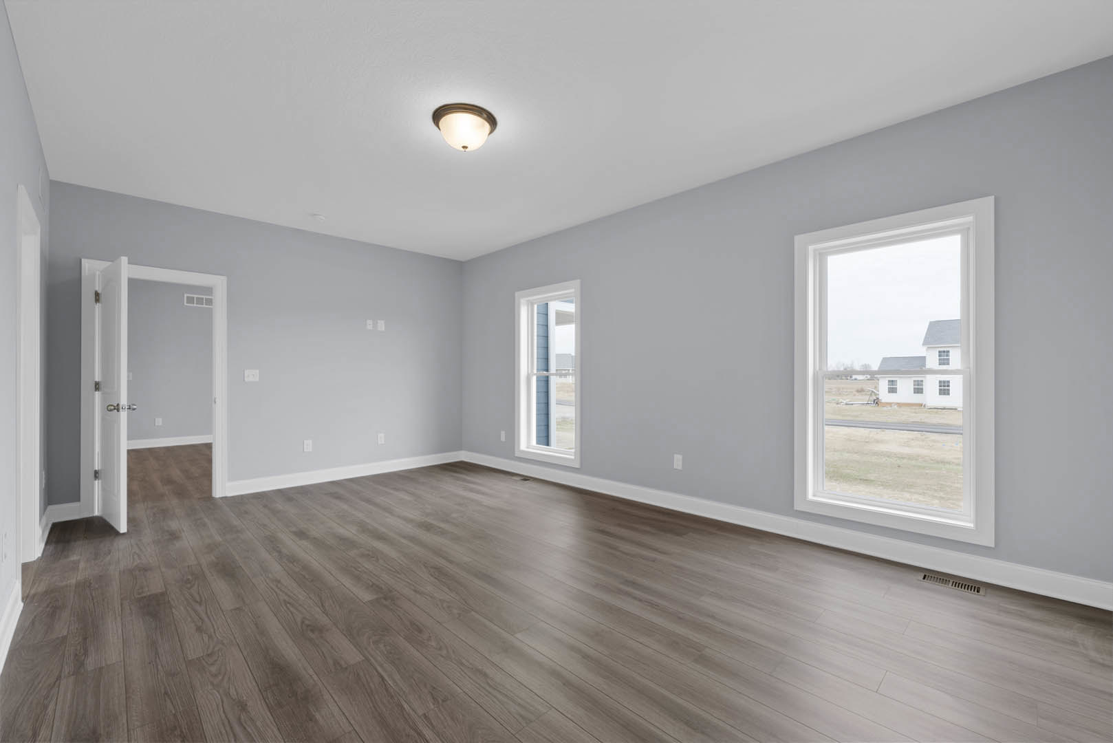 Spacious room with wood flooring, large windows, blue accent wall, white door with silver knobs, and modern ceiling light fixture