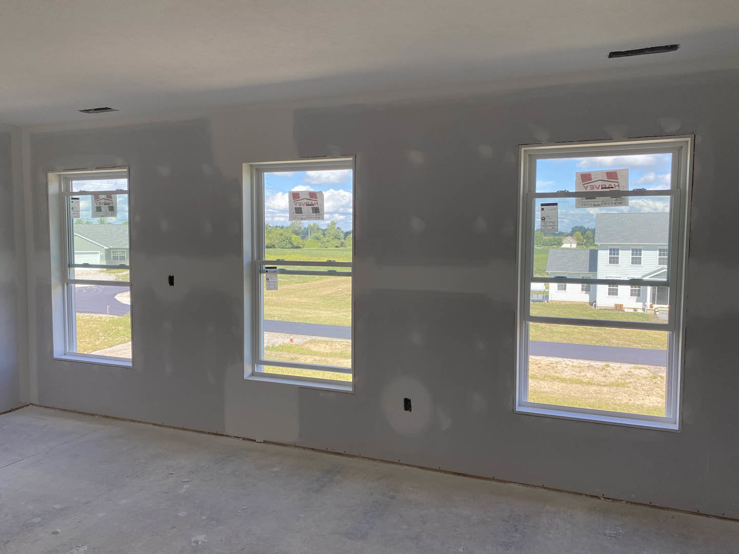 Spacious room with large windows overlooking grassy field, concrete floor, gray walls, and ceiling fixtures