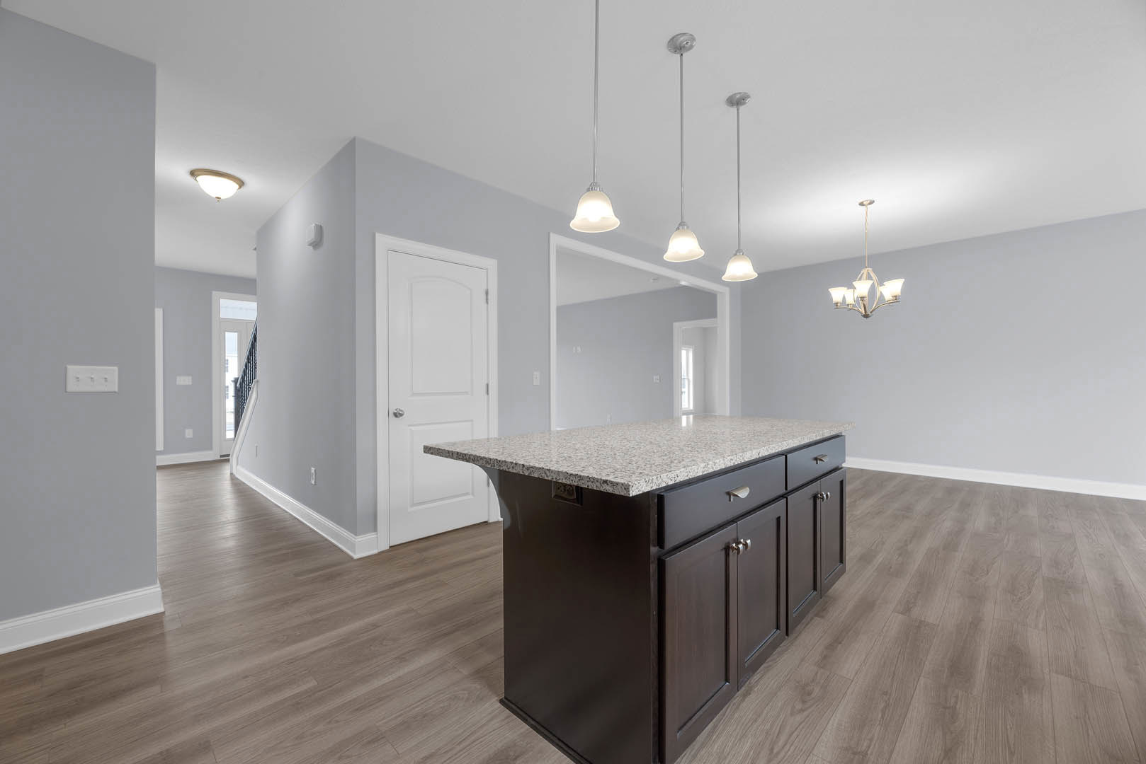 Granite kitchen island with white cabinetry, marble countertop, stainless steel sink, light switch and electrical outlet on nearby wall, hardwood flooring