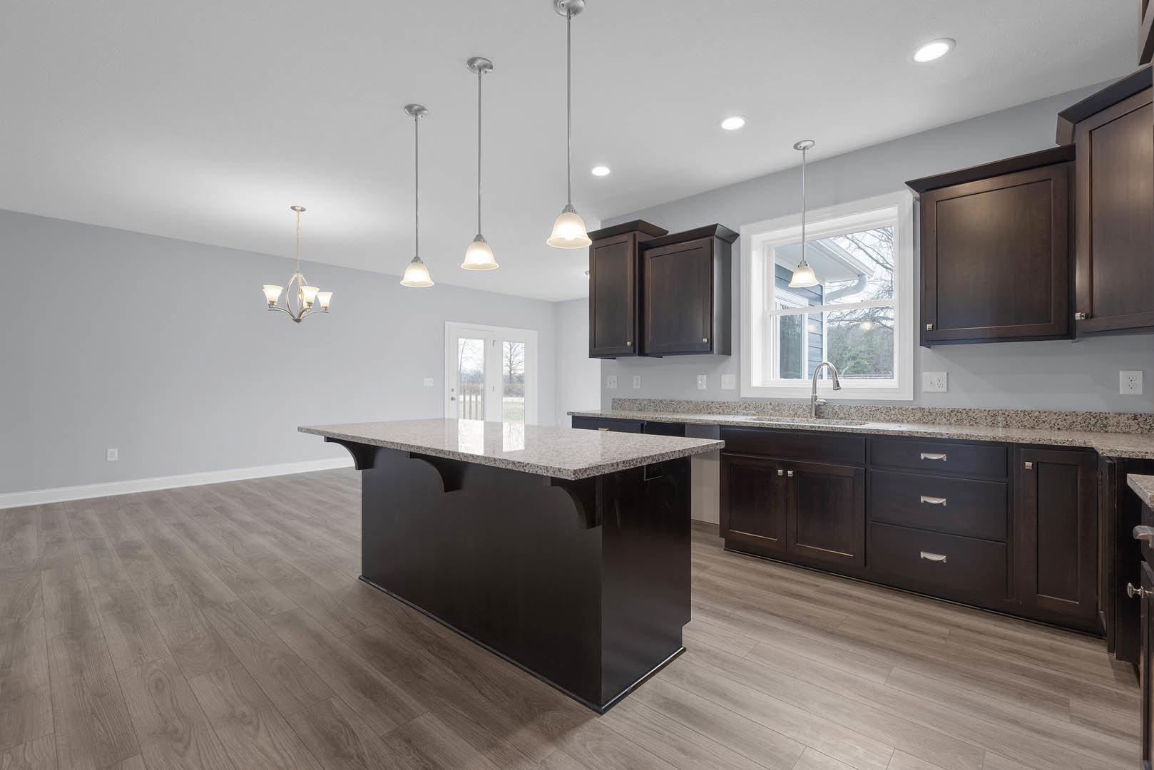 Open kitchen with wood flooring, central island featuring black cabinetry and marble countertop, stainless steel sink under modern pendant light, white walls, and sleek faucet.
