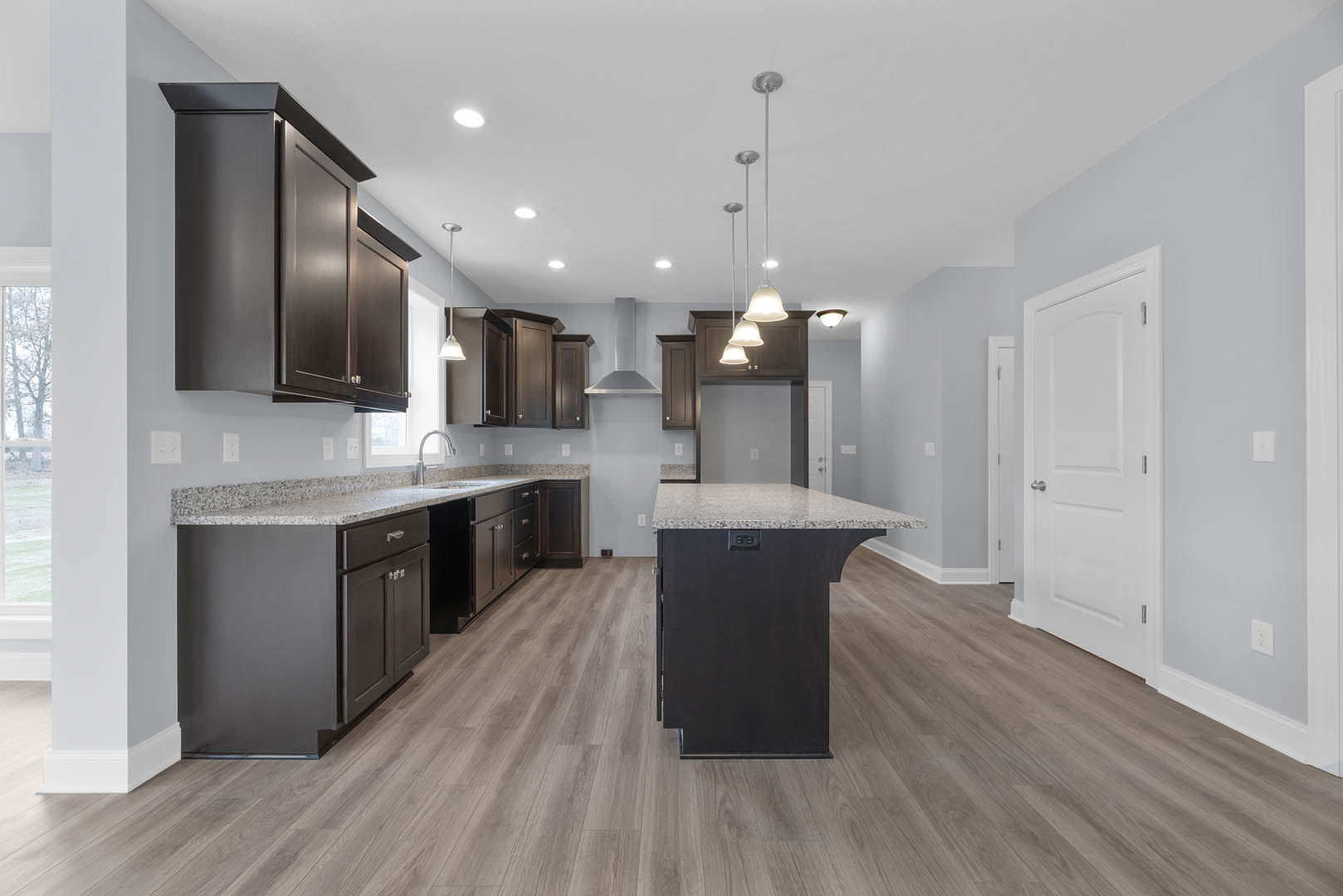Kitchen with dark wood cabinets, granite countertops, marble island, stainless steel faucet, and white door with silver knob