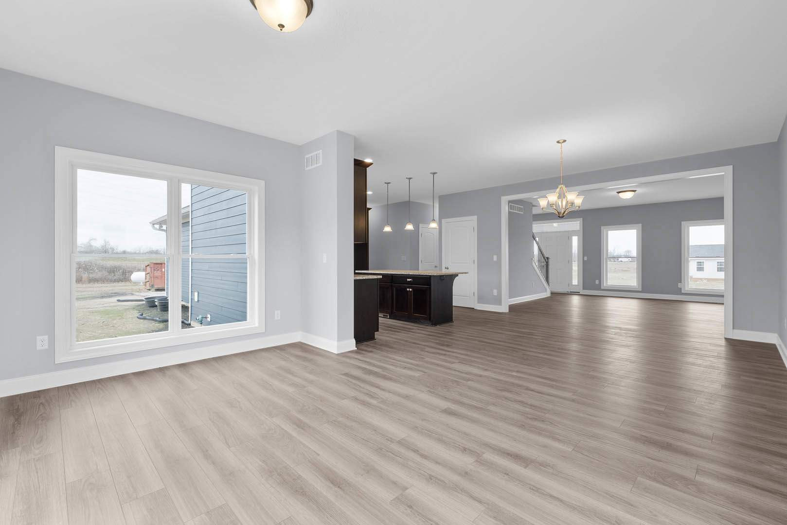 Open concept room with hardwood flooring, black kitchen island topped with marble, large window overlooking yard, modern light fixture, plaster walls, and white ceiling.