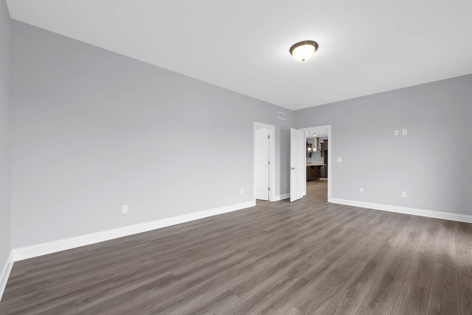 Wood flooring with white baseboards, white door featuring silver handle and metal hinge, ceiling-mounted light fixture, smooth plaster walls.