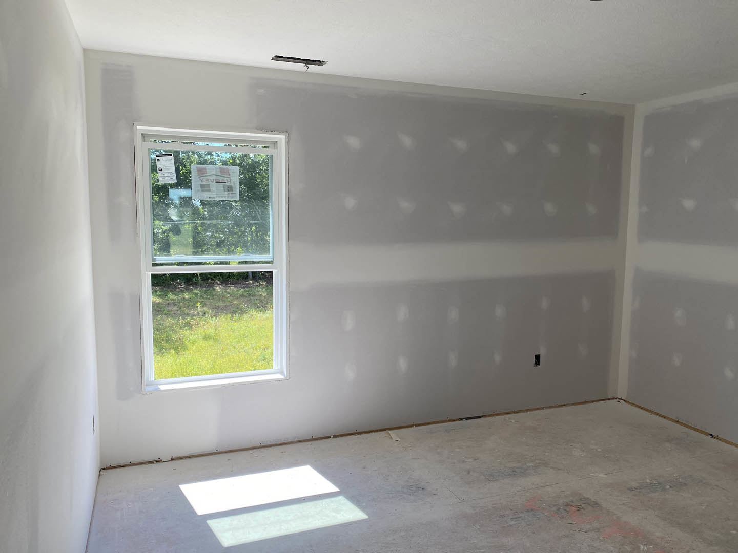 Bright room with two large windows, white plaster walls, light wood flooring, and a newspaper taped to one window.