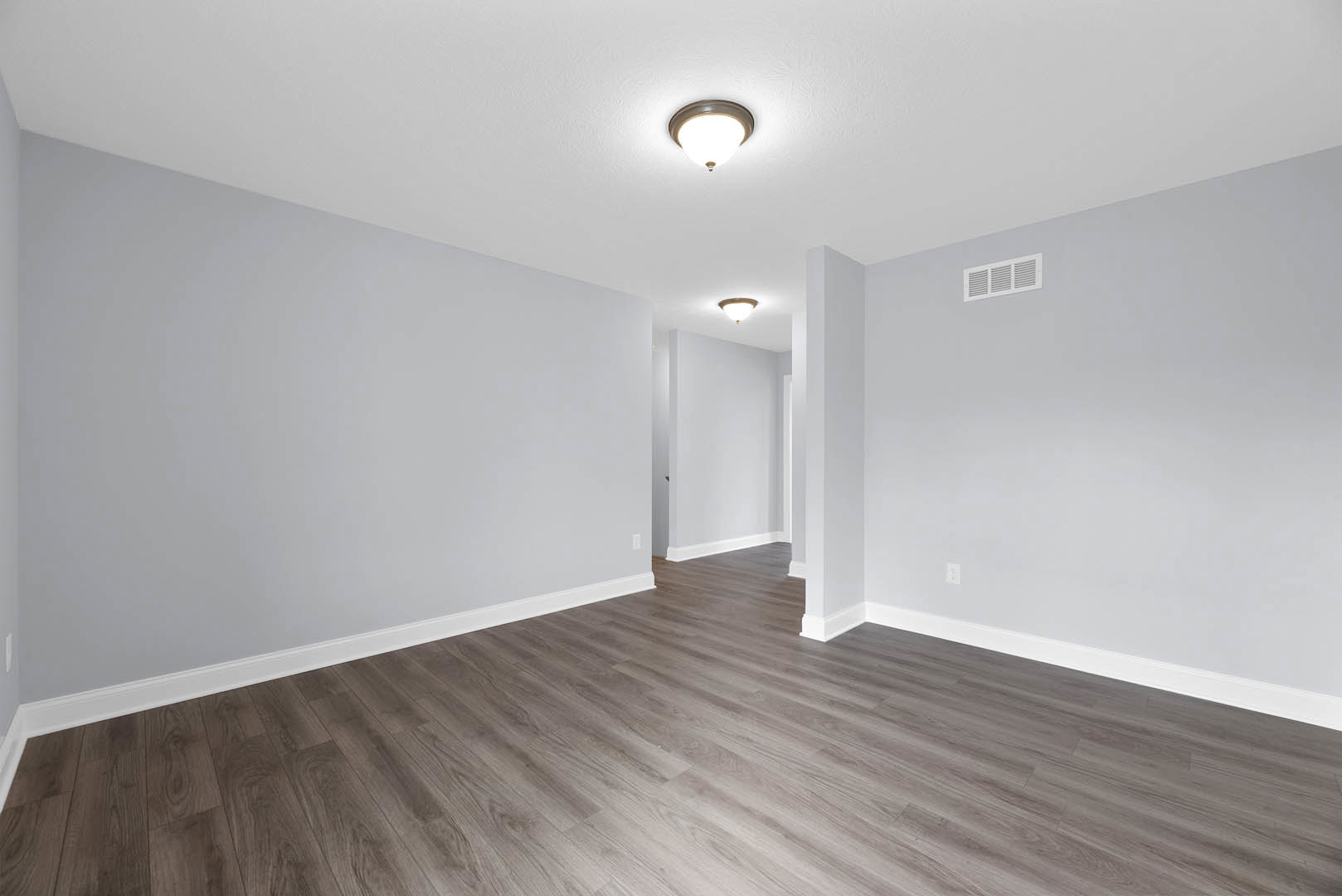 Hardwood floor room with white walls, ceiling-mounted light fixture, and wall vent