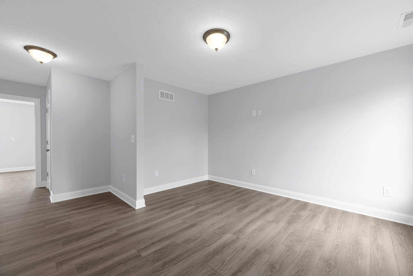 Wood flooring in a room with white plaster walls, ceiling vent, light switch, and a modern ceiling fixture.