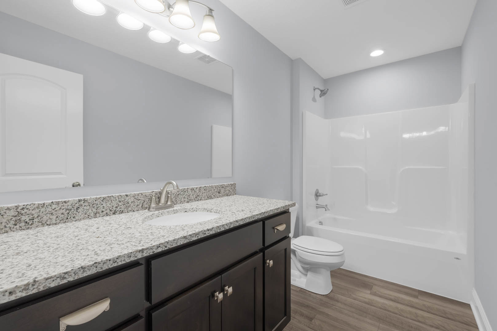 Modern bathroom with white porcelain sink and toilet, glass-enclosed shower, gray tile flooring, white cabinetry, quartz countertop, and arched doorway.