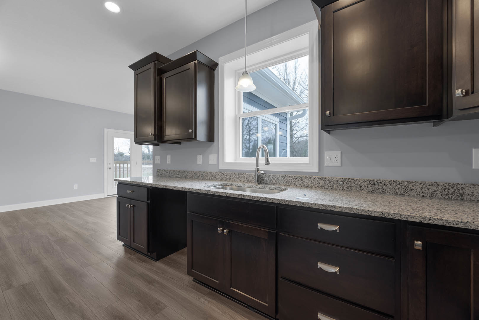 Kitchen featuring dark wood cabinets, polished granite countertops, stainless steel faucet, and drawers; natural light streams through a window above the sink.
