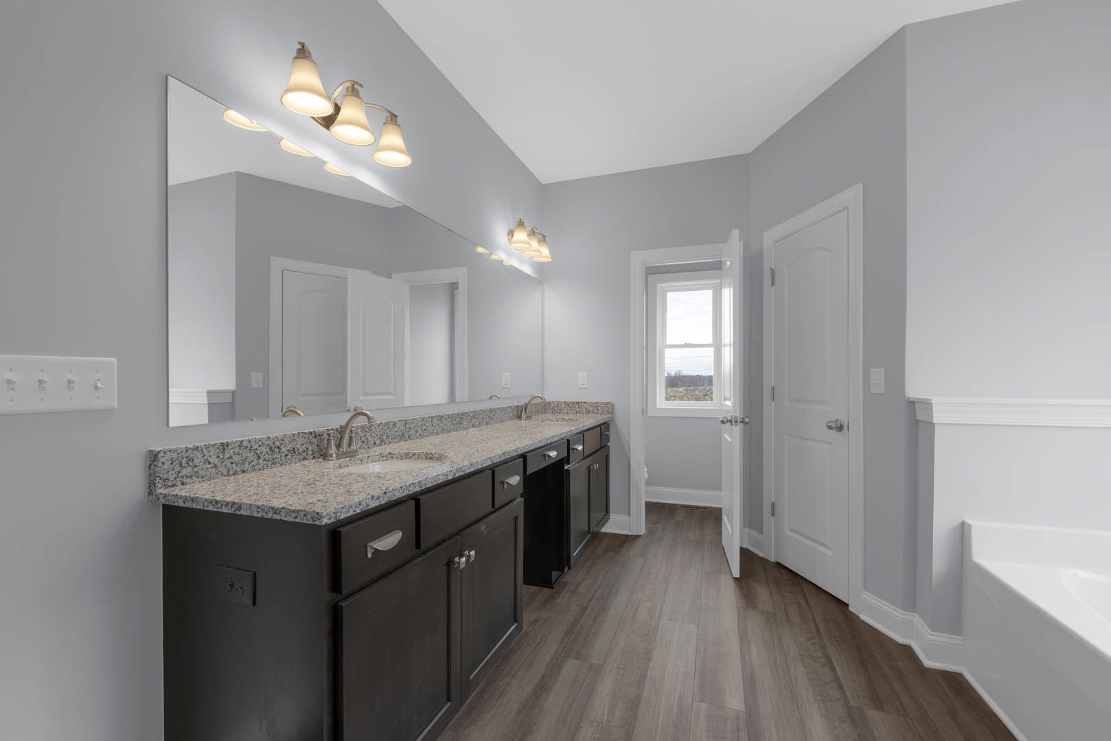 Bathroom featuring marble countertop, wood flooring, white door with silver handle, wall-mounted metal towel holder, ceiling light fixture, white bathtub, and sink with cabinetry