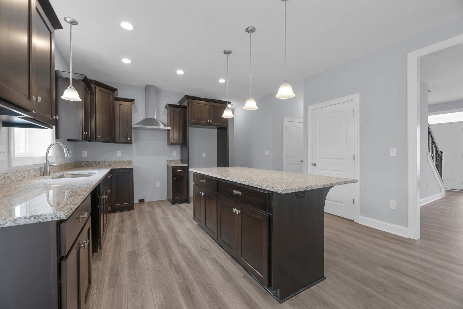Spacious kitchen featuring a large central island with granite countertops, white cabinetry, stainless steel appliances, pendant lighting, and light wood flooring.