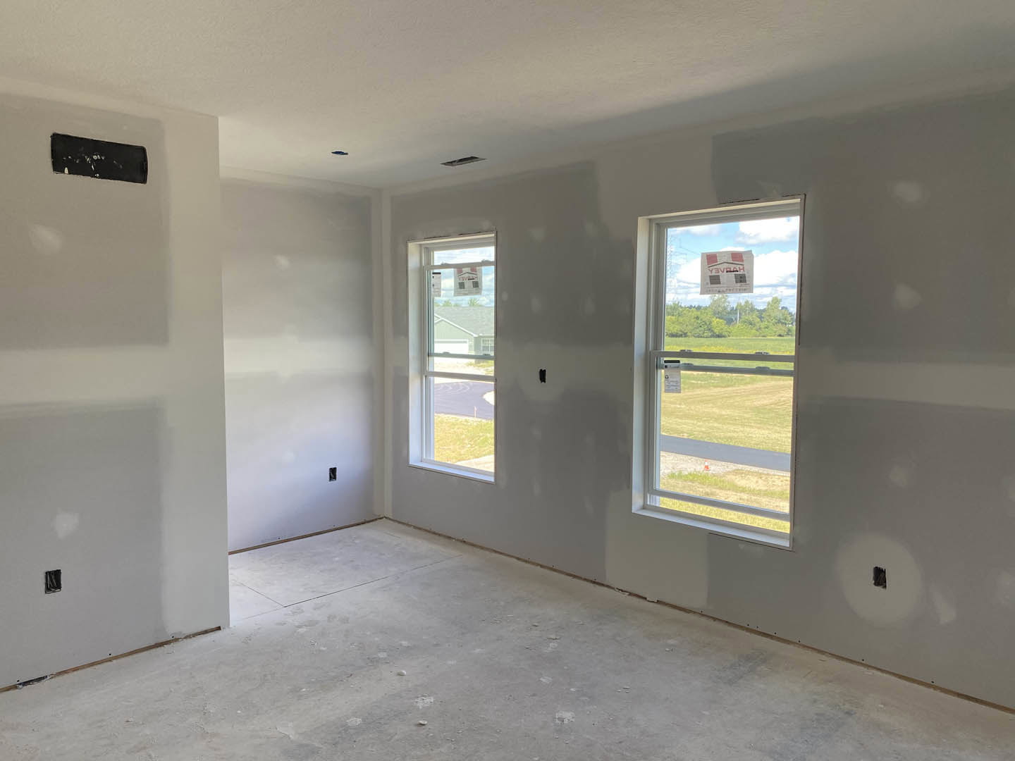 Bright room with two large windows, smooth plaster walls, light wood flooring, and a black rectangular fixture near the wall.