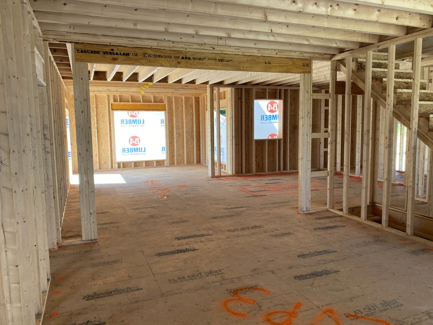 Living room with exposed wood ceiling beams, large window, orange-painted floor, and wooden sign displaying black numbers and letters.