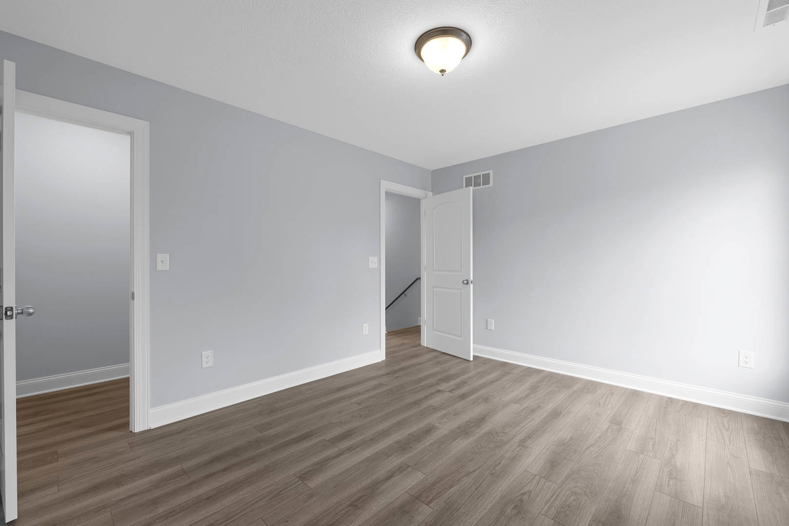 White paneled door with silver knobs, wood flooring with white base trim, black handrail, ceiling light fixture, smooth plaster walls