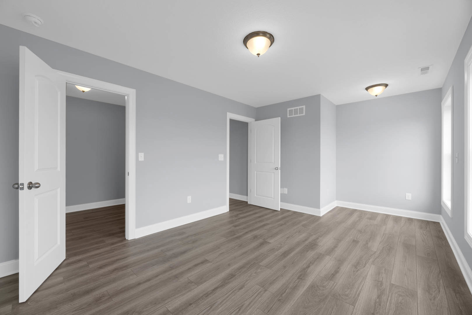 White paneled door with silver knobs, wood laminate flooring, white baseboard trim, ceiling-mounted light fixture illuminated, smooth plaster walls