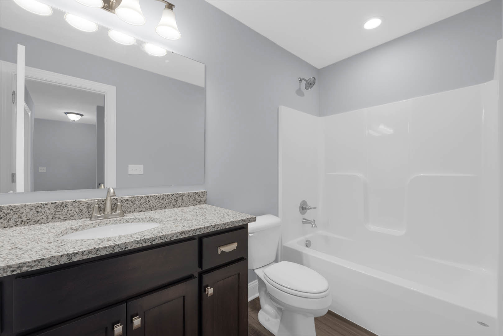 White porcelain sink with chrome faucet set in a light stone countertop, adjacent to a modern toilet; wall-mounted shower head visible, large format gray tile walls, under-cabinet