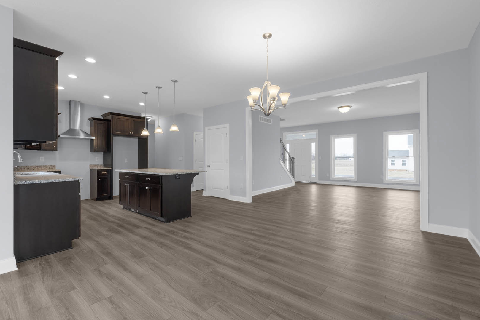 Spacious open-concept kitchen featuring a central island with drawers, black marble countertop, hardwood flooring, white cabinetry, silver hardware, and large windows with exterior