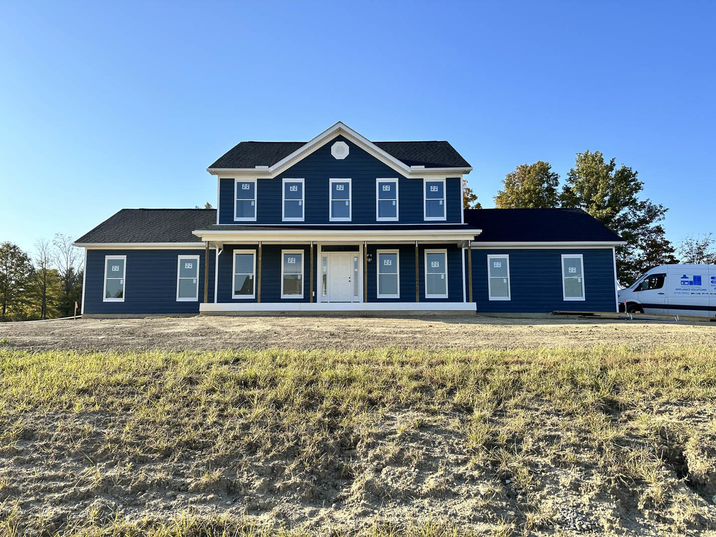 Blue house with white trim, glass panel door, grassy lawn, mature trees in background, white van parked nearby