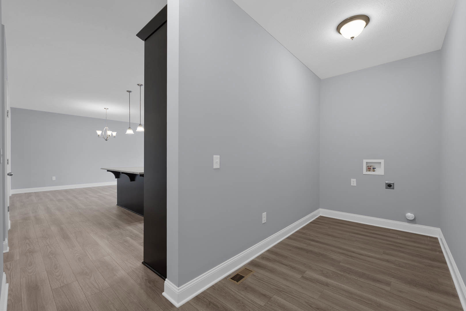 Wood flooring in a room featuring a matte black cabinet, white walls, recessed ceiling light, floor vent, and a door; open shelving holds containers.