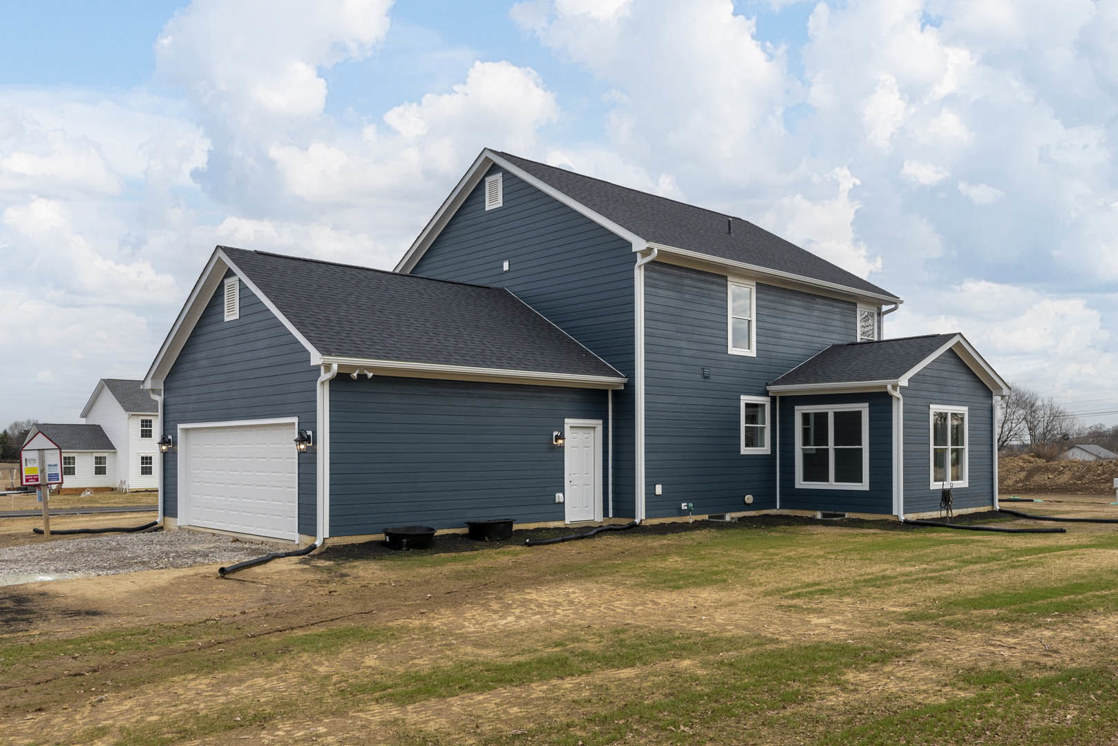 Two-story house with light siding, attached garage, white doors, white-framed windows, green lawn, and blue sky with clouds