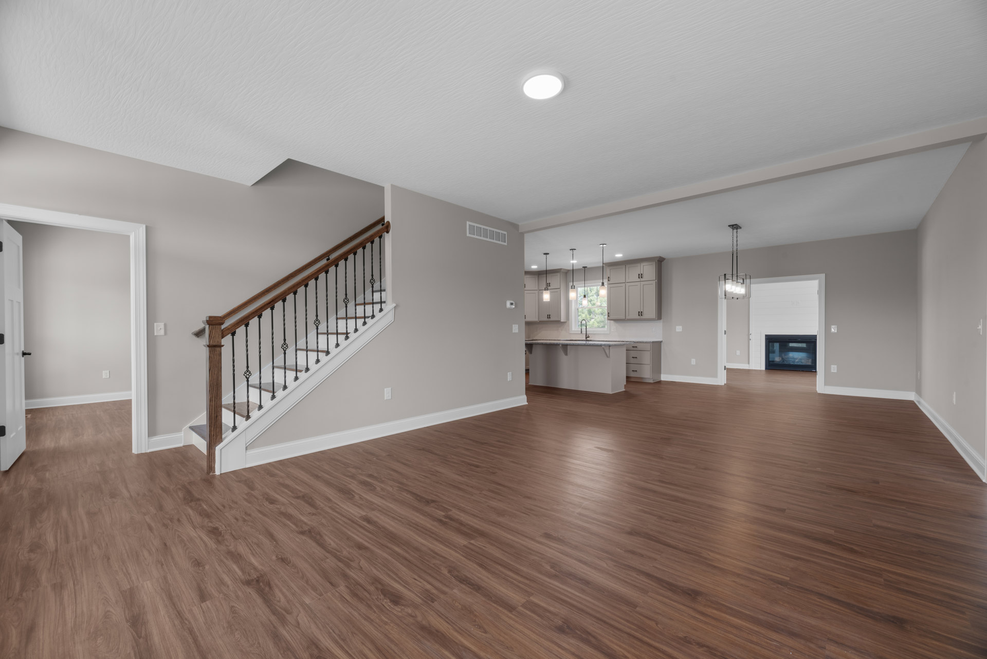 Spacious empty room with hardwood floors, wood staircase with railings, ceiling light fixture, and glass door with black frame
