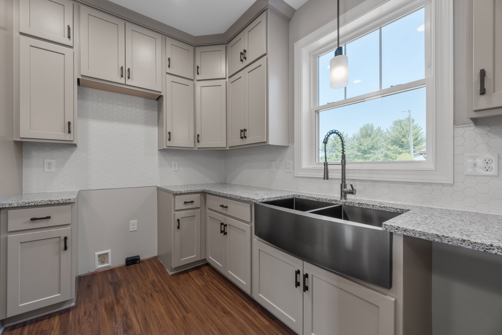 Modern kitchen featuring a stainless steel sink with chrome faucet beneath a large window, white cabinetry with black handles, light-colored countertops, and built-in appliances.