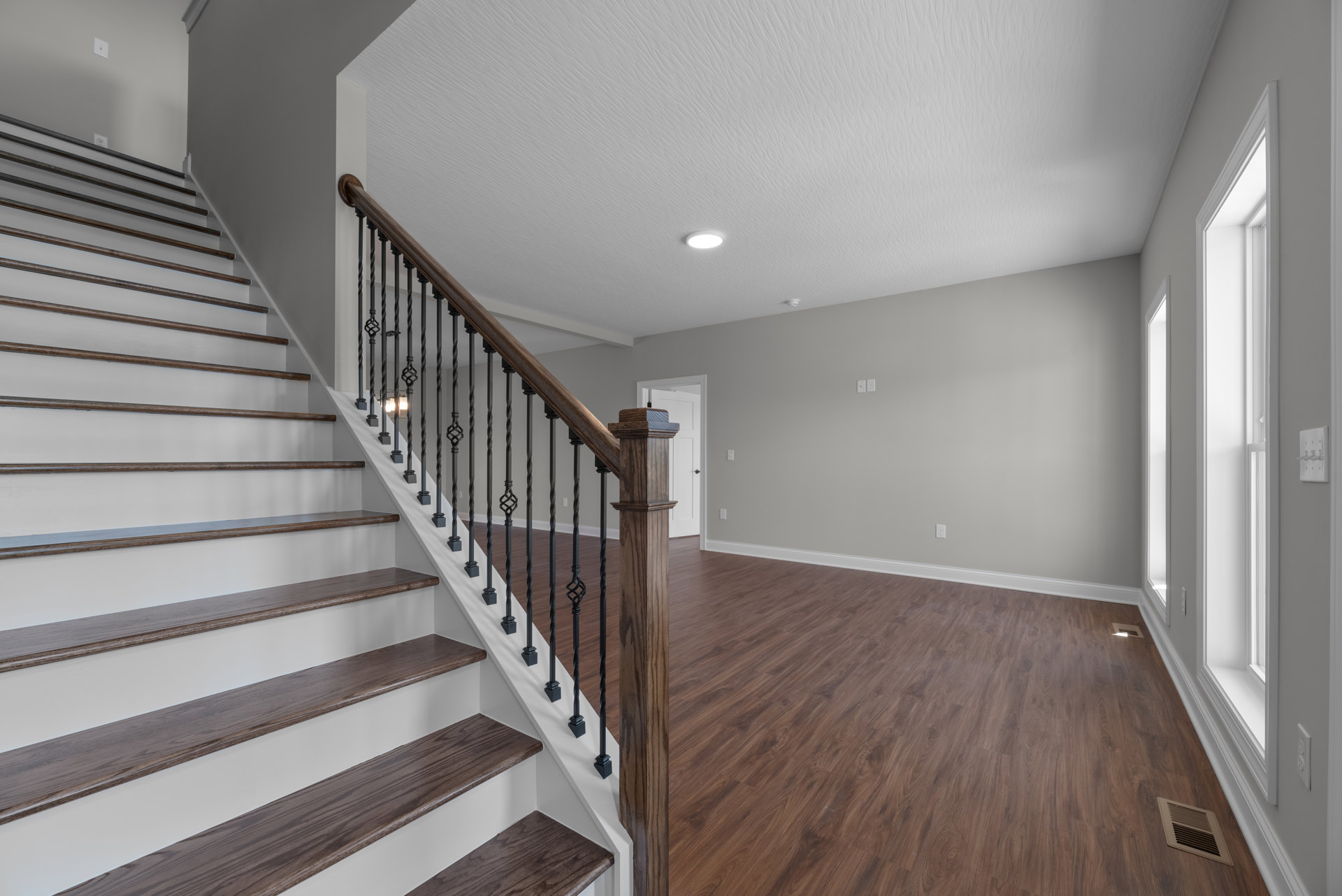 Wood staircase with matching handrails and balusters, laminate flooring, white plaster walls, and a vent set into the stair riser