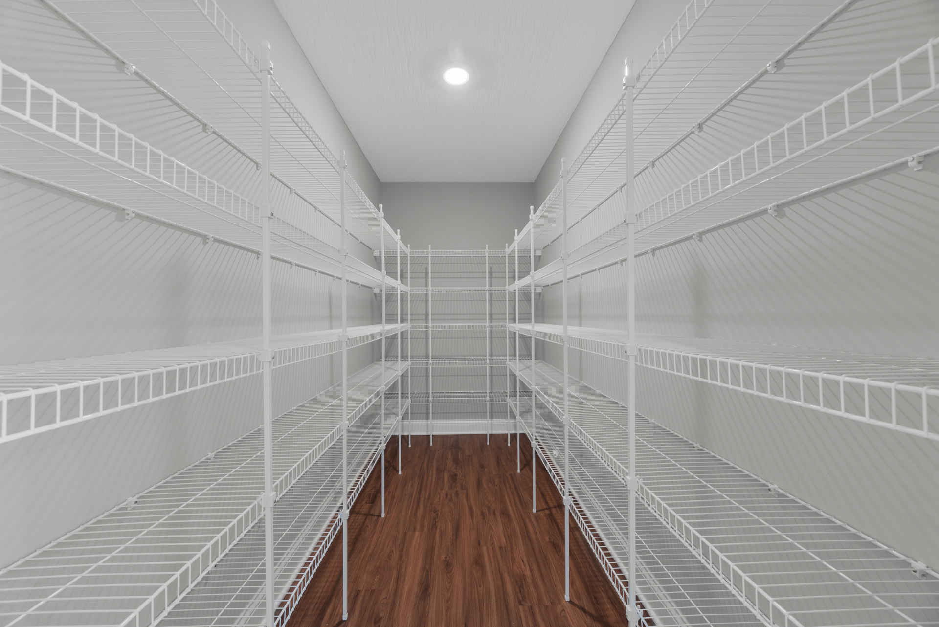 White built-in shelves line the wall of a room with light wood flooring, plaster walls, and a ceiling light fixture; stairs with a wood handrail are visible.