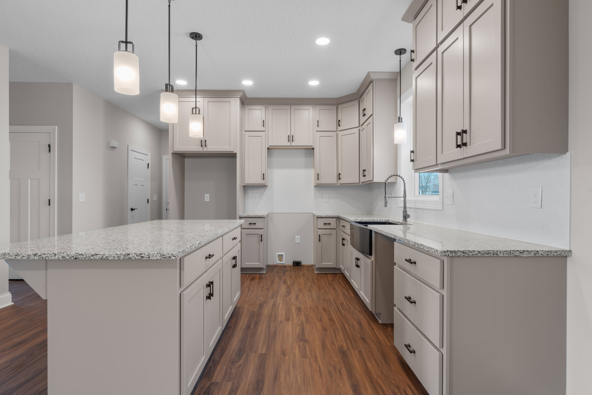 White shaker cabinets, stainless appliances, wood plank flooring, quartz countertop, undermount sink, brushed metal pendant light, and chrome faucet in a modern kitchen.